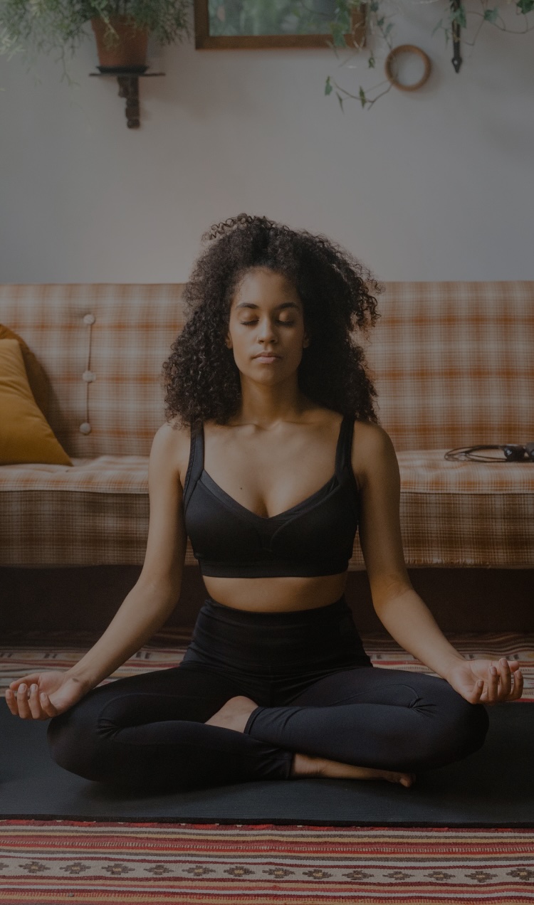 A woman meditates with her eyes closed on a black yoga mat.