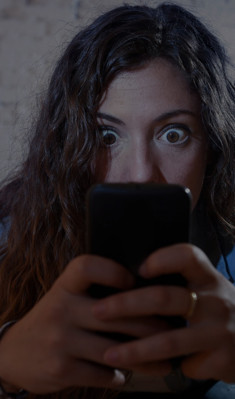 A woman clutches her phone with her eyes gazing intensely at the screen.