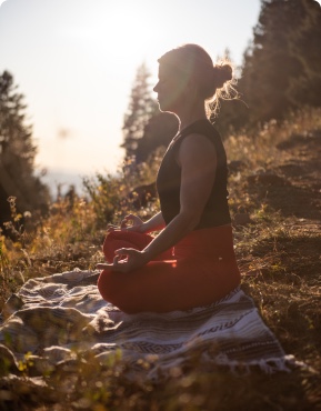 A woman sits with her legs crossed in lotus pose as she meditates on the mountain.