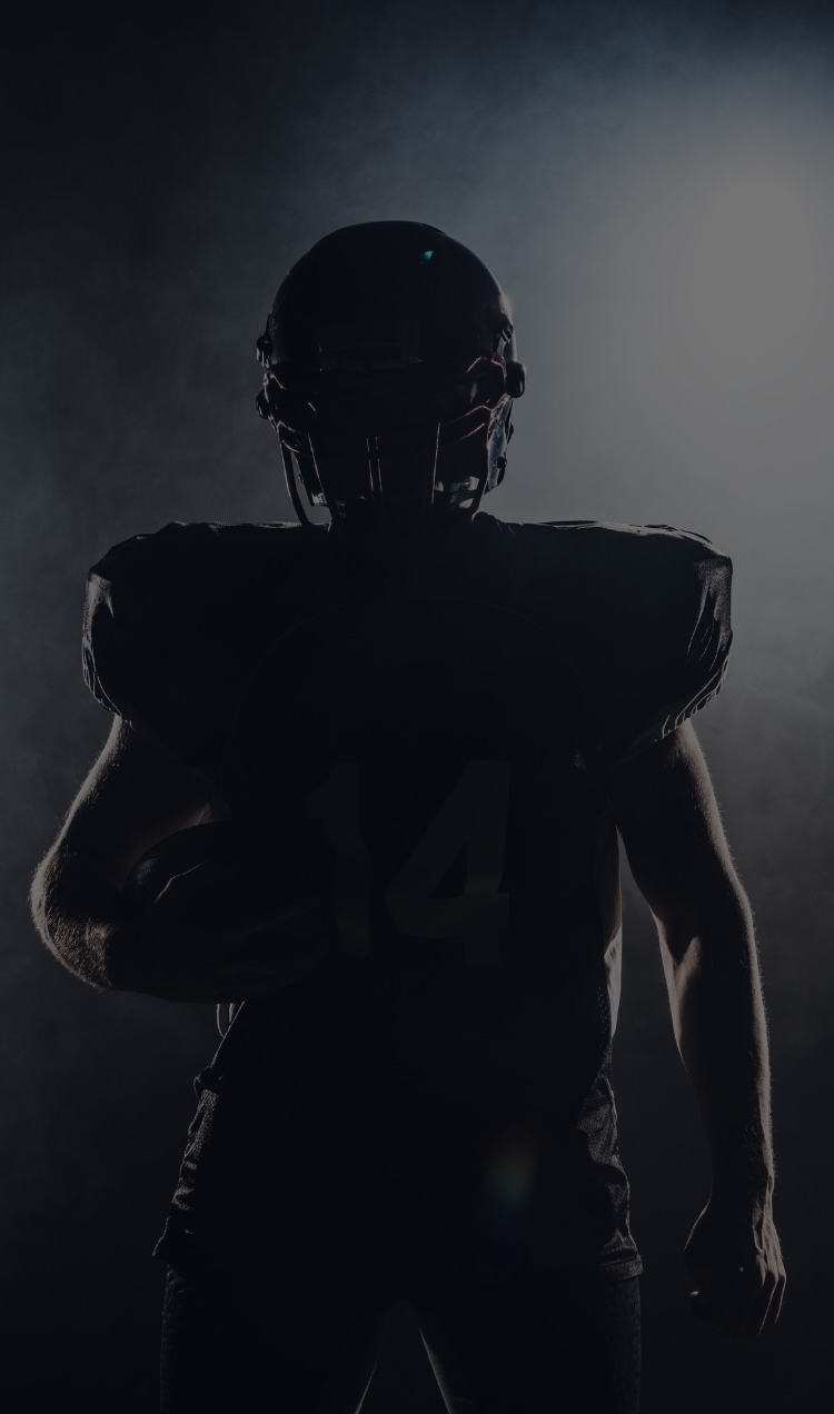 A football player stands on the field in shadows.