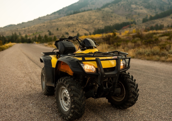 A yellow and black ATV on a trail in front of the mountains.