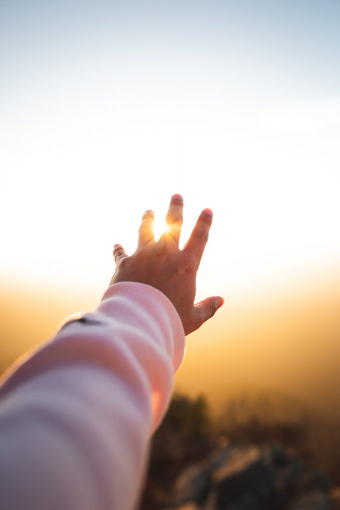 A hand reaching out to the sun over the horizon.
