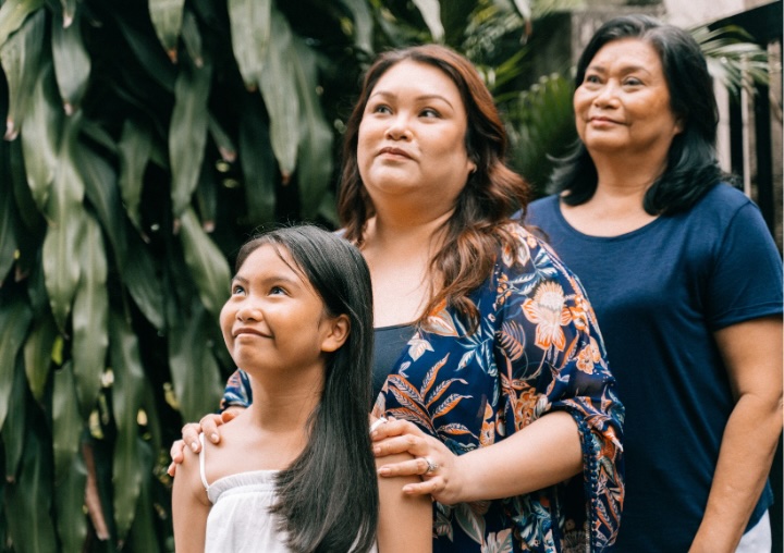 Three generations of women (grandmother, mother, and daughter) smiling for a family photo.