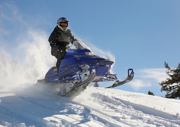 A snowmobiler jumps onto a hill.