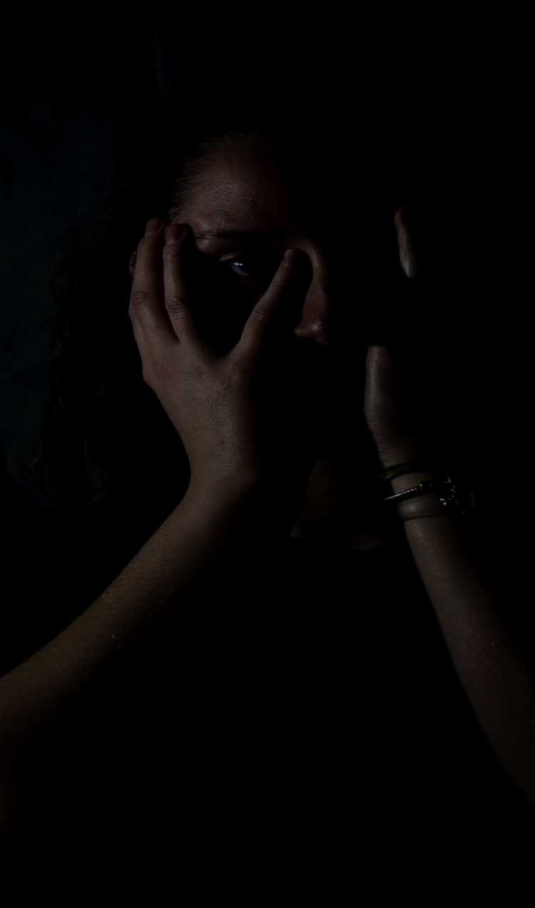 A person holds their face in a dark room.