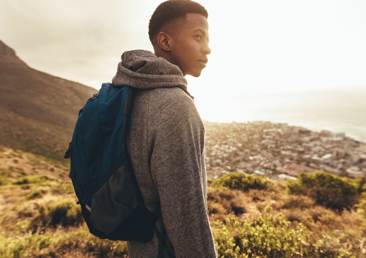 A man wearing a backpack overlooks a valley while on a hike.