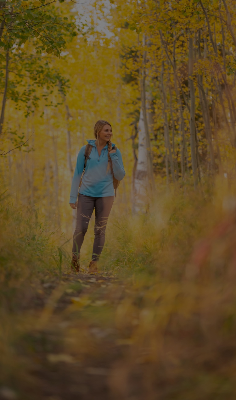 A woman in a blue jacket hikes through a trail in Colorado surrounded by golden Aspen trees.