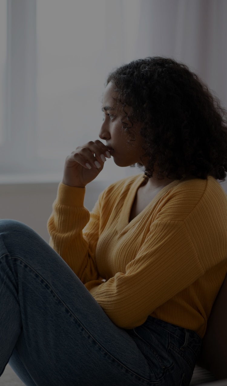 A woman sits on the couch with her hand resting on her lips, looking a bit disconnected.