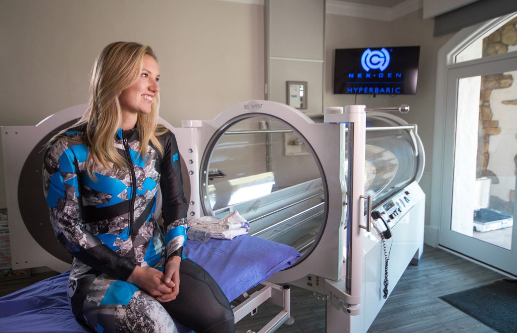 An Olympic-hopeful athlete sits on the bed of a hyperbaric chamber at All Points North Lodge.