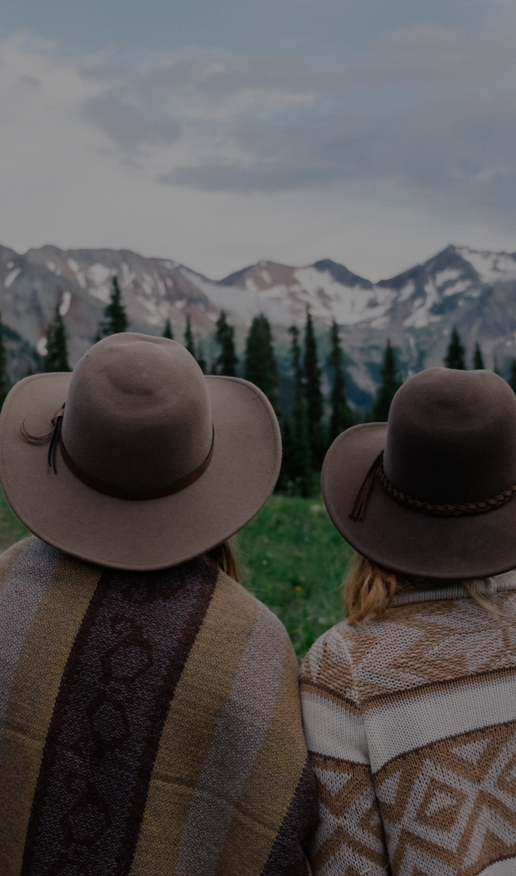 A couple sits in a green field overlooking the Colorado mountains.