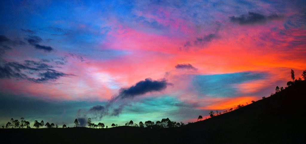 A multicolored sunset over a dark hill.