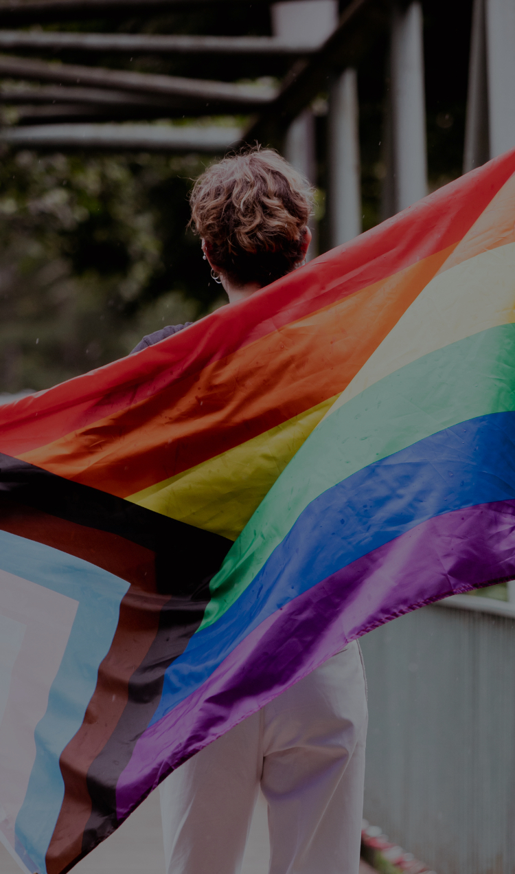 A person marches with an inclusive pride flag flowing behind them.