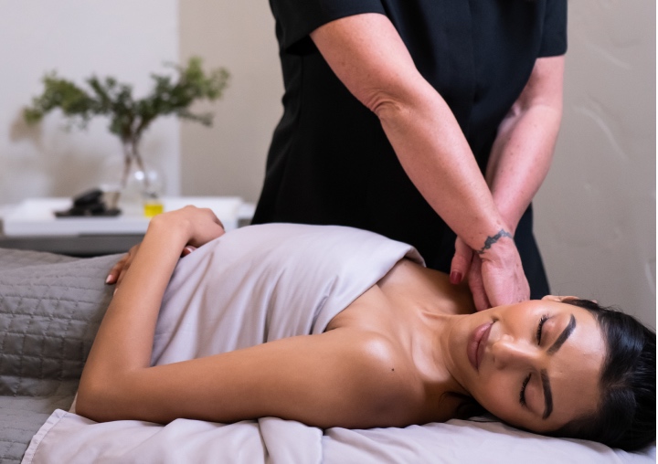 A woman lays on a massage table while a masseuse works on her shoulder.