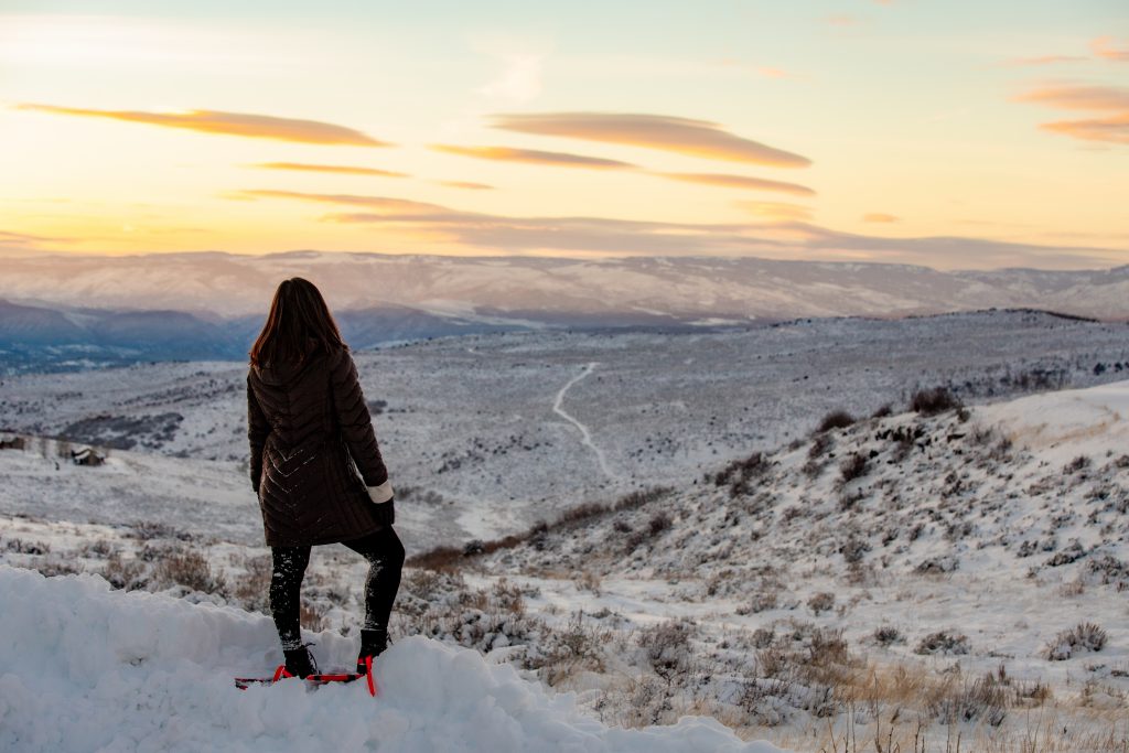 A woman stands at the top of a hill, overlooking the snowy Colorado landscape below.