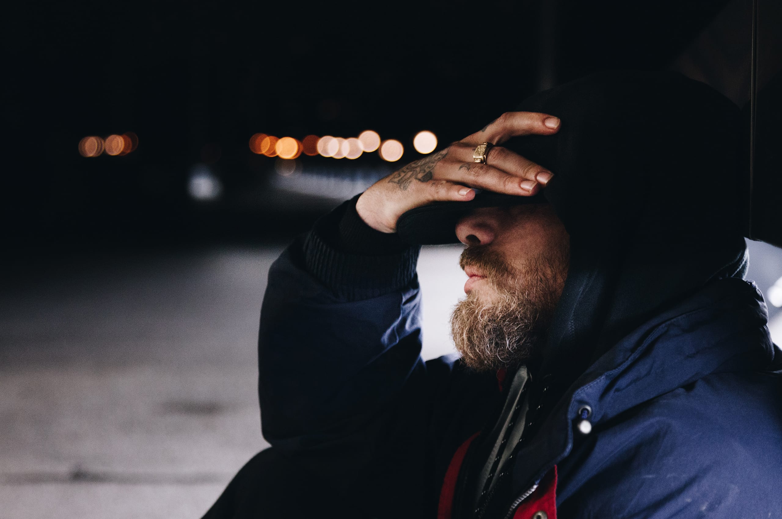 man sitting on the curb at night with hand on forehead