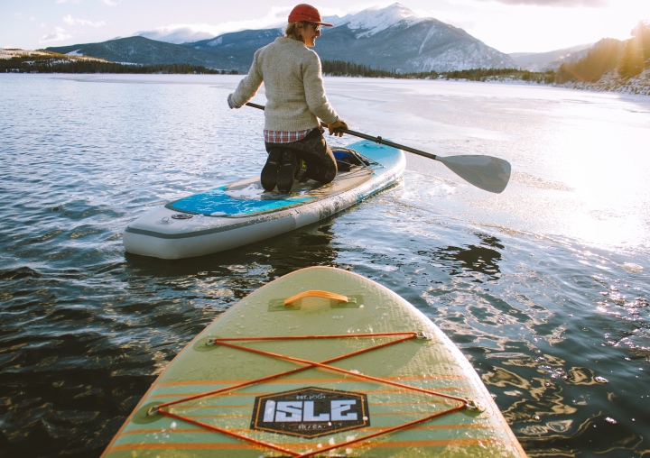 A client paddle boards with the sun setting over the mountains.