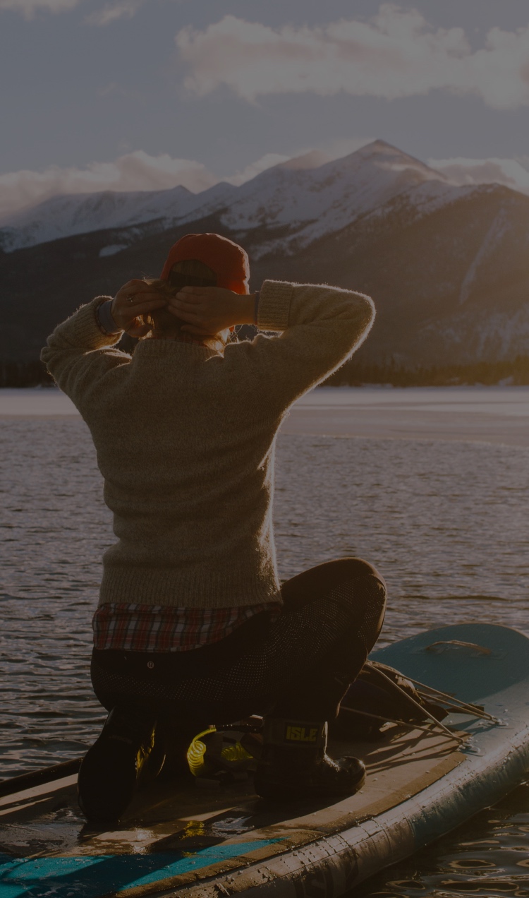 A client paddleboards as the sun sets over the mountains.