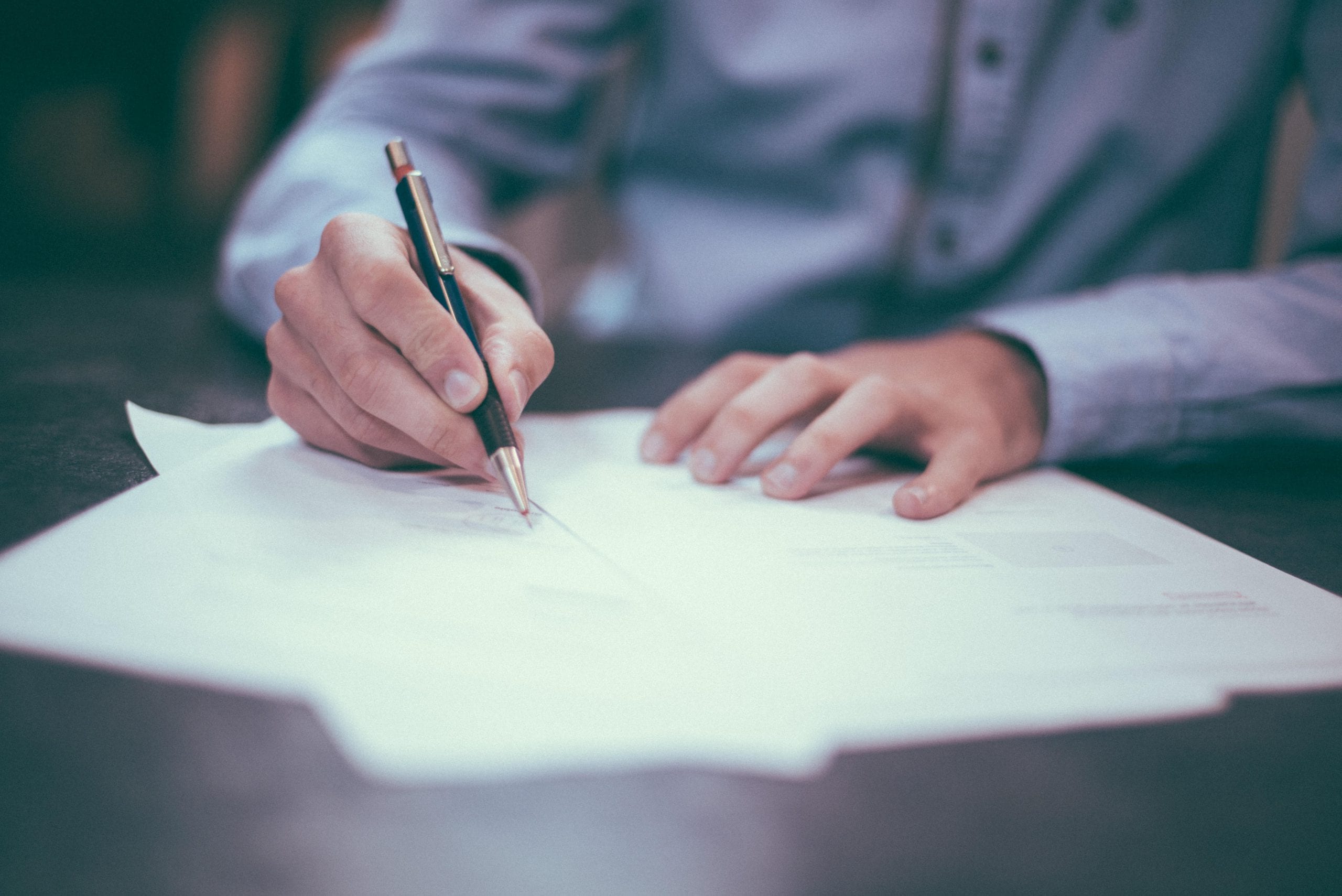 man writing on papers with a pen