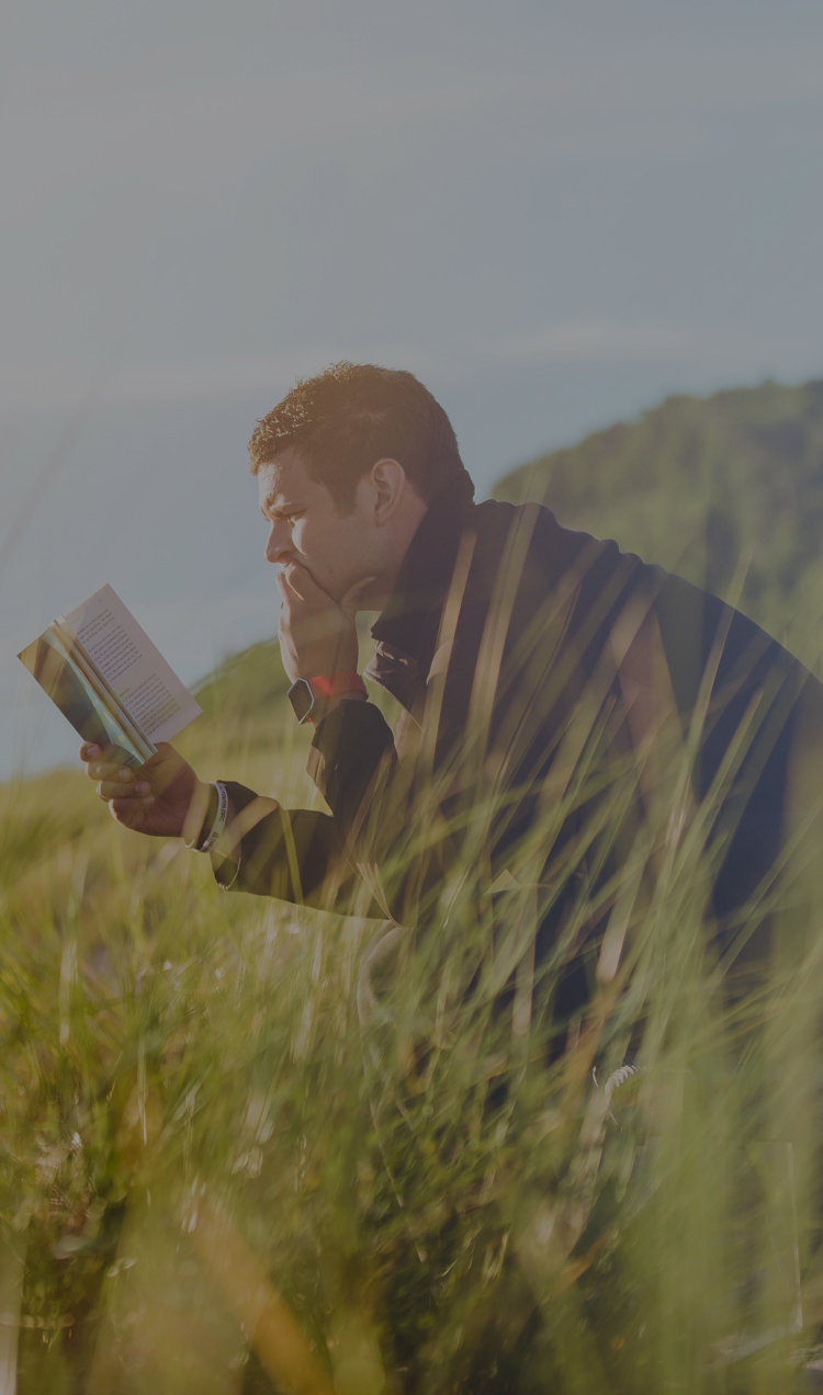 A man reading in a field overlooking a cliff.