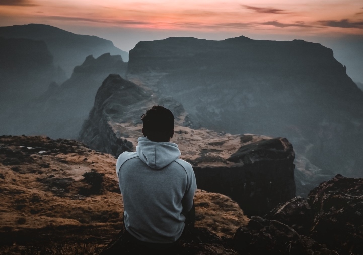 Man Sitting on Cliff Watching Sunset