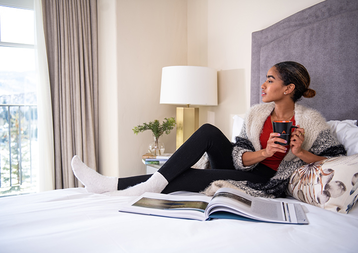 Woman relaxing on a bed with a hot beverage and magazine