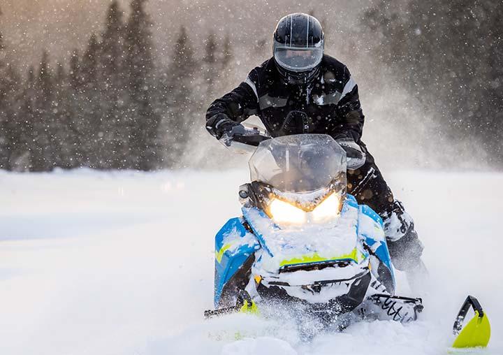 Someone snowmobiling across an open plain with pine forest in the background