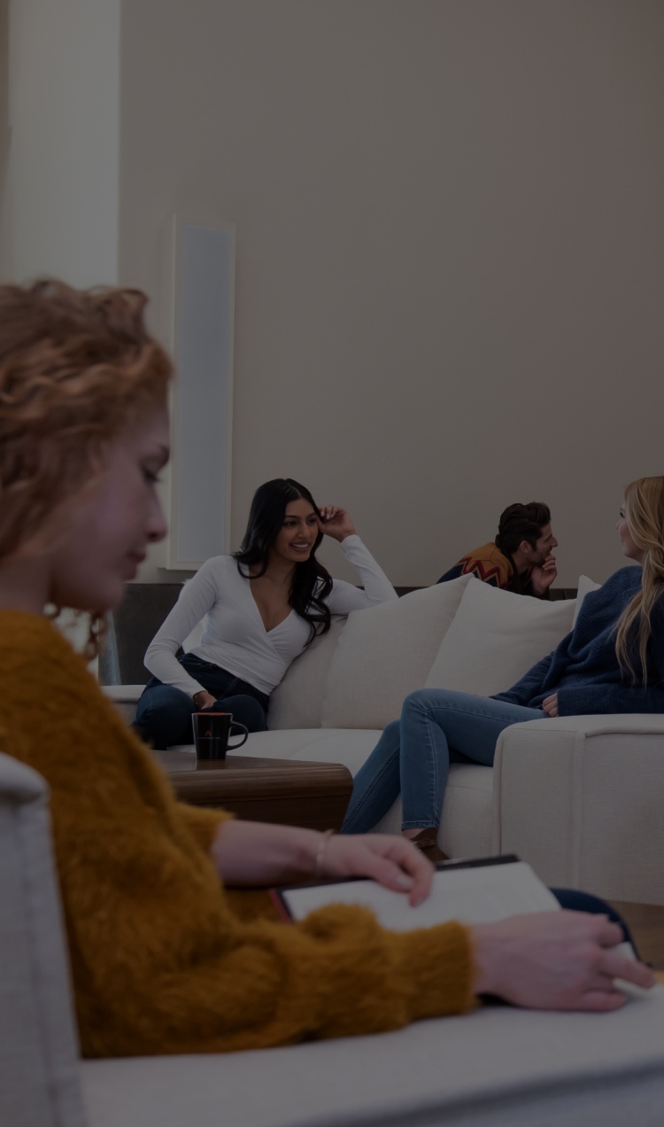 Woman reading on a couch with other people talking to each on couches in the background