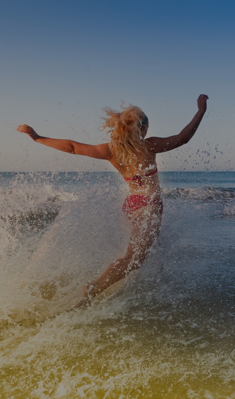 A woman splashes into the waves with her arms raised in the air.