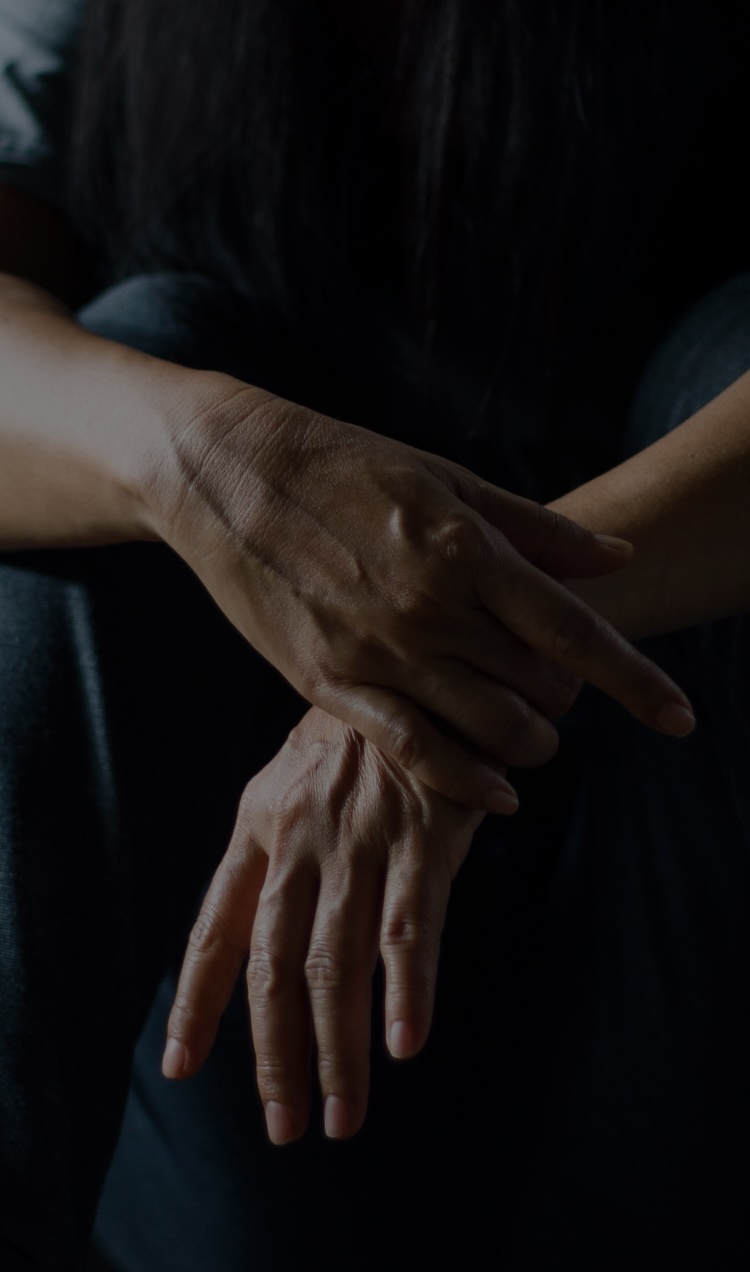 A person sitting on the ground in a dark room with their hands crossed.