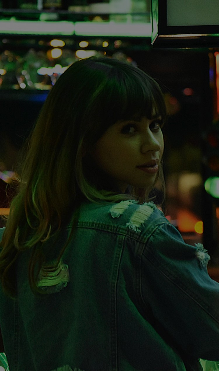 A woman stands at a bar and looks back over her shoulder.