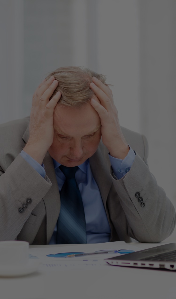 A man holds his head in his hands at his desk in a toxic workplace.