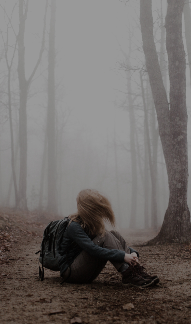 A person sits on a trail in the misty woods with their hair falling in their face.