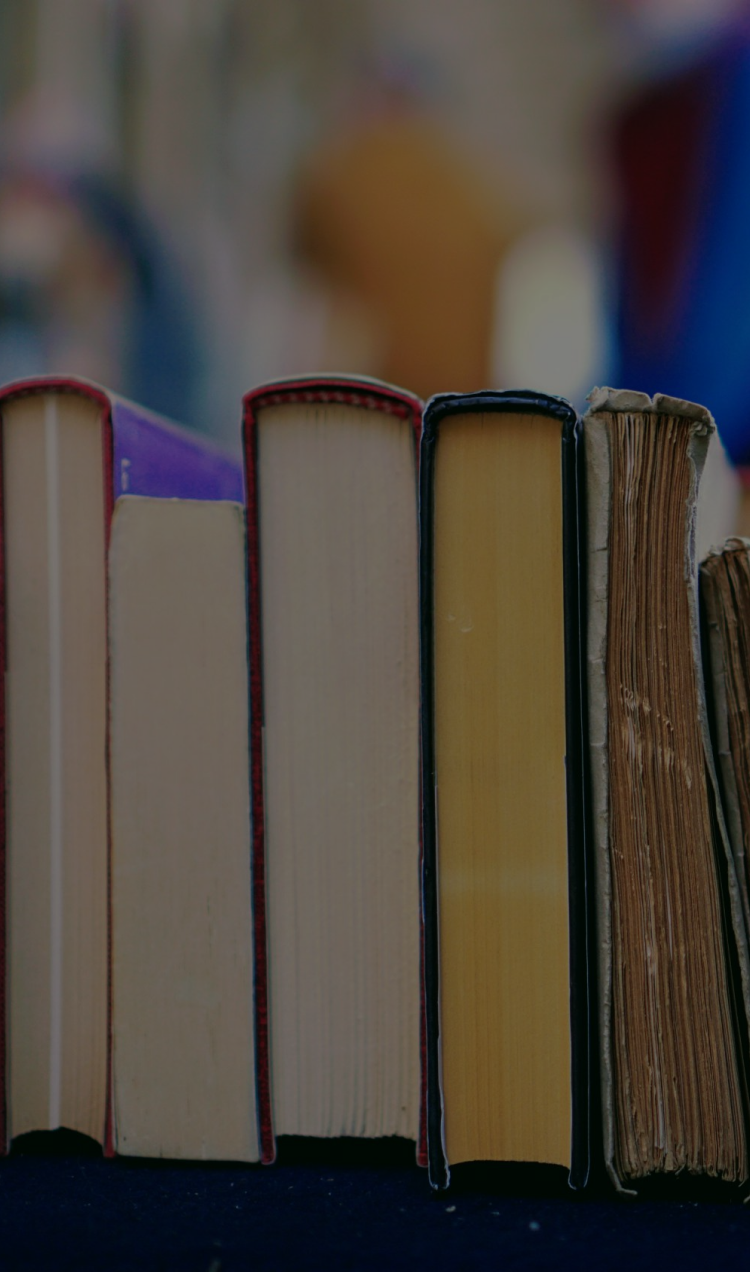 A side view of a stack of books piled on a cart with the spines facing up.