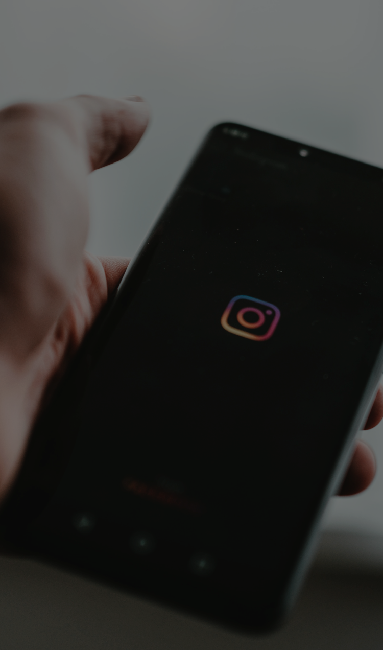 A man holds an iPhone with a black screen and the rainbow Instagram logo in the center.