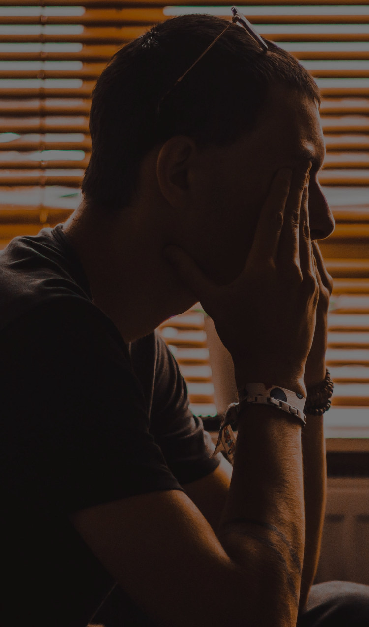 A man sits, visibly frustrated, with his head in his hands in a dim room.