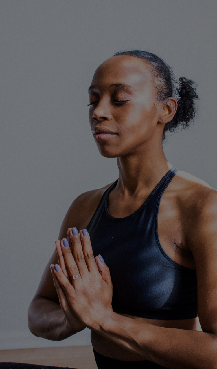 A woman sits in lotus pose with prayer hands with her eyes closed.