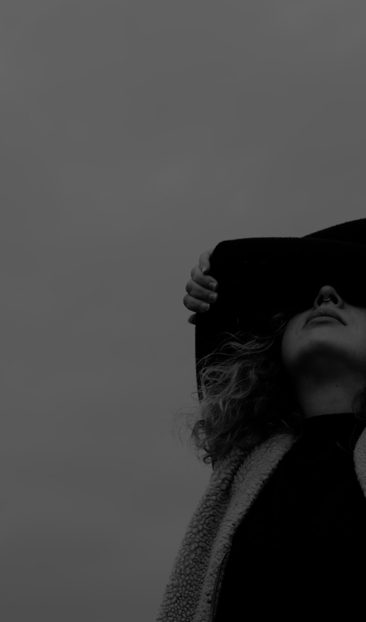 A black and white photo of a woman with both arms crossed and resting on top of her head, blocking her vision.