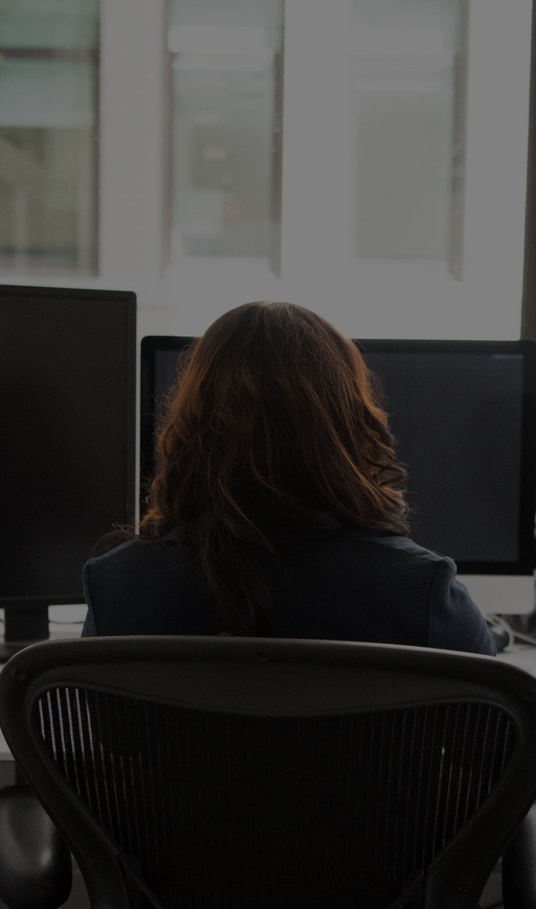 A woman sits in front of her computer desk at work.