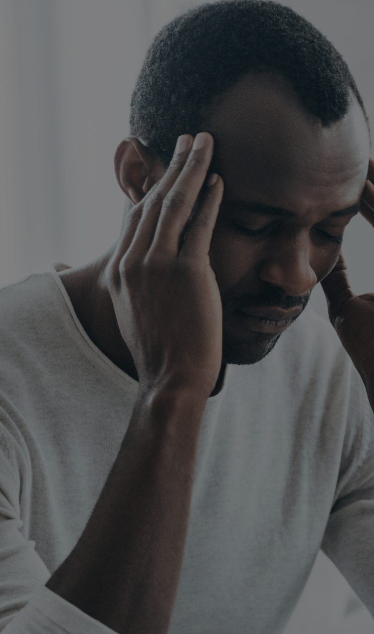 A man holds his head with both hands as he sits in pain in a bright white room.