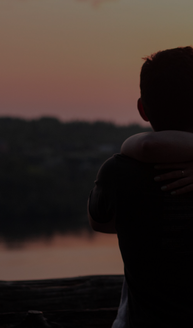 A couple embraces each other with a sunset in the background.