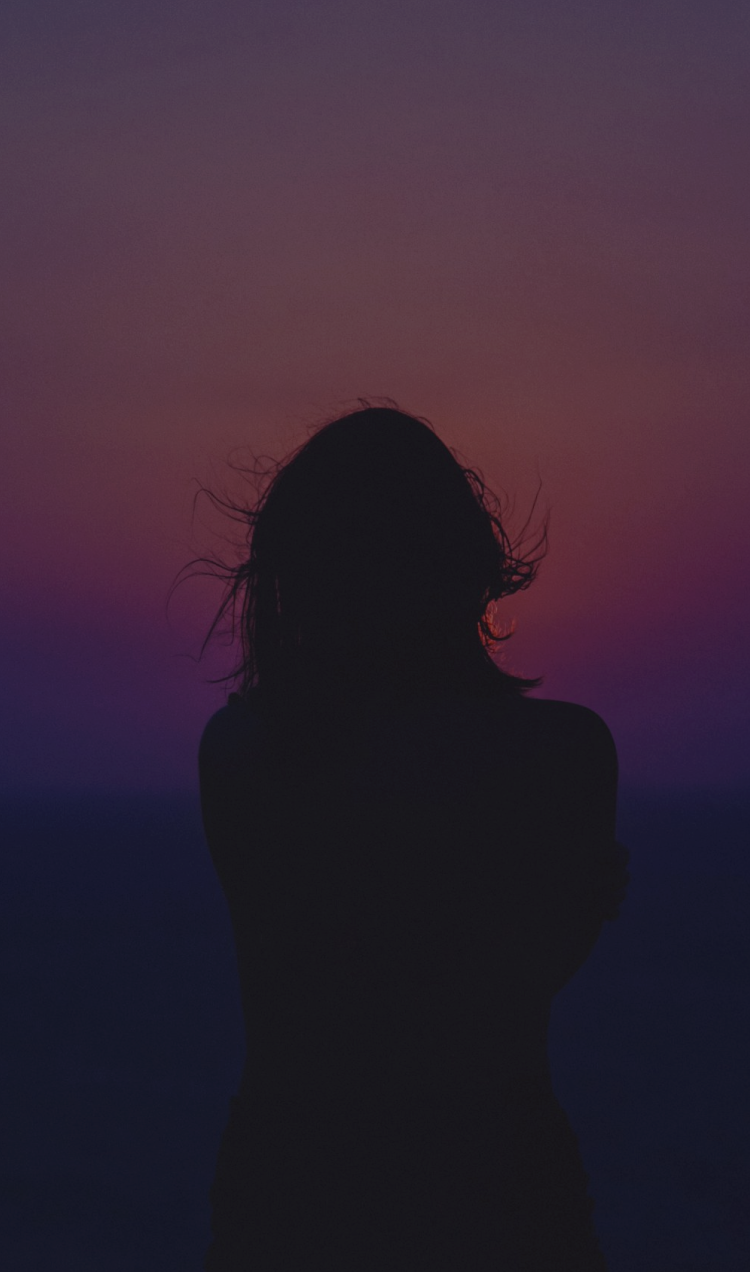 Silhouette of a woman facing a pink and purple sunset.