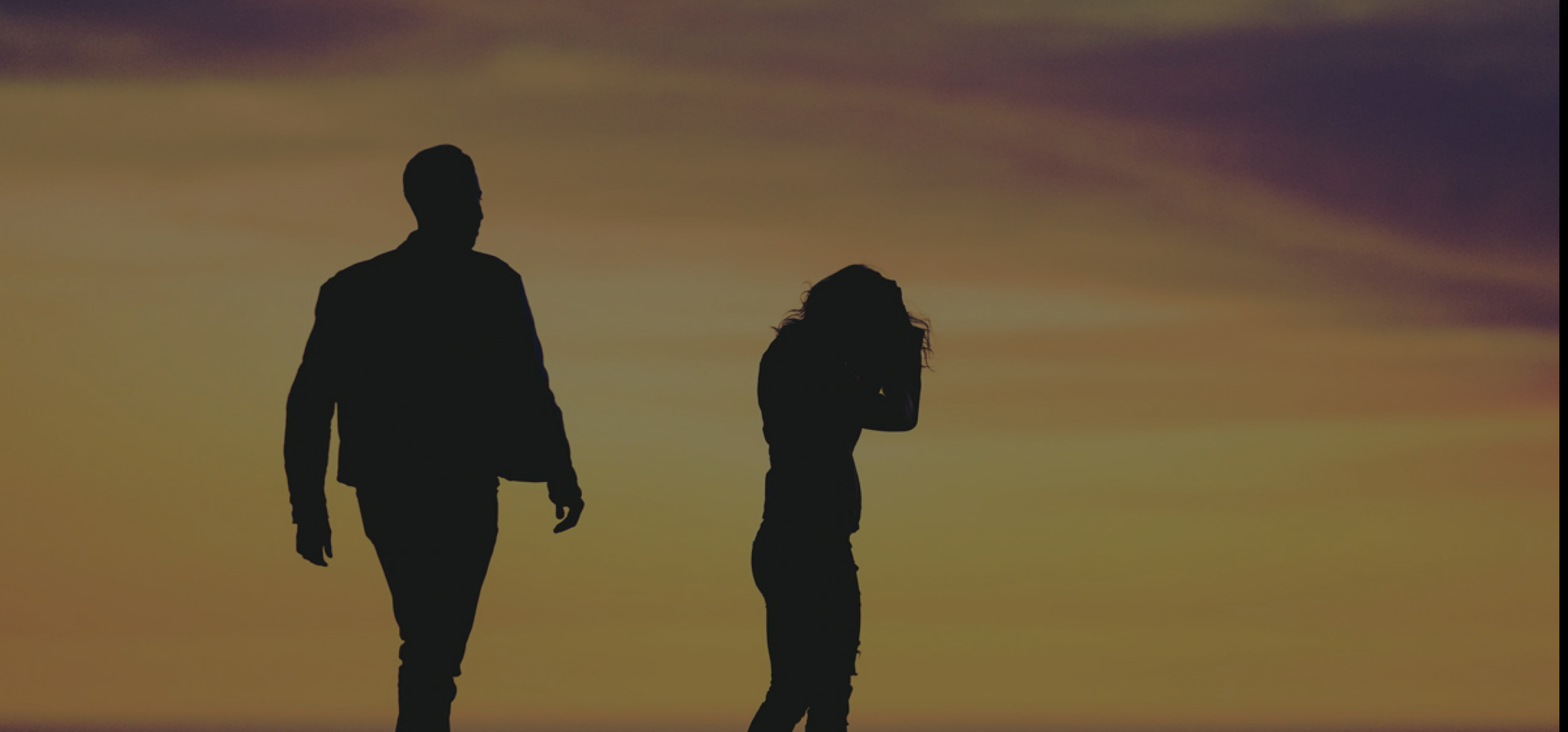 A silhouette of a distant couple on the beach backlit by the sunset.
