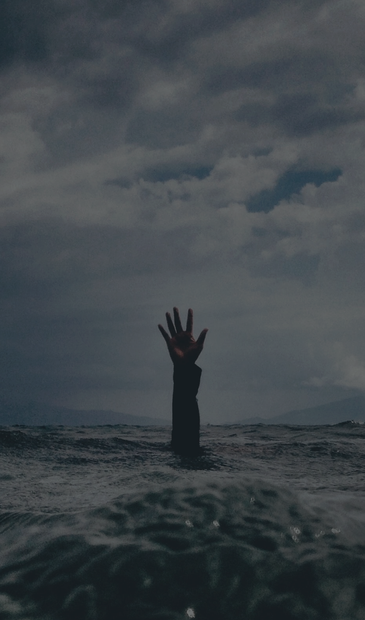 Someone under the water in an ocean with their hand reaching out of the waves.