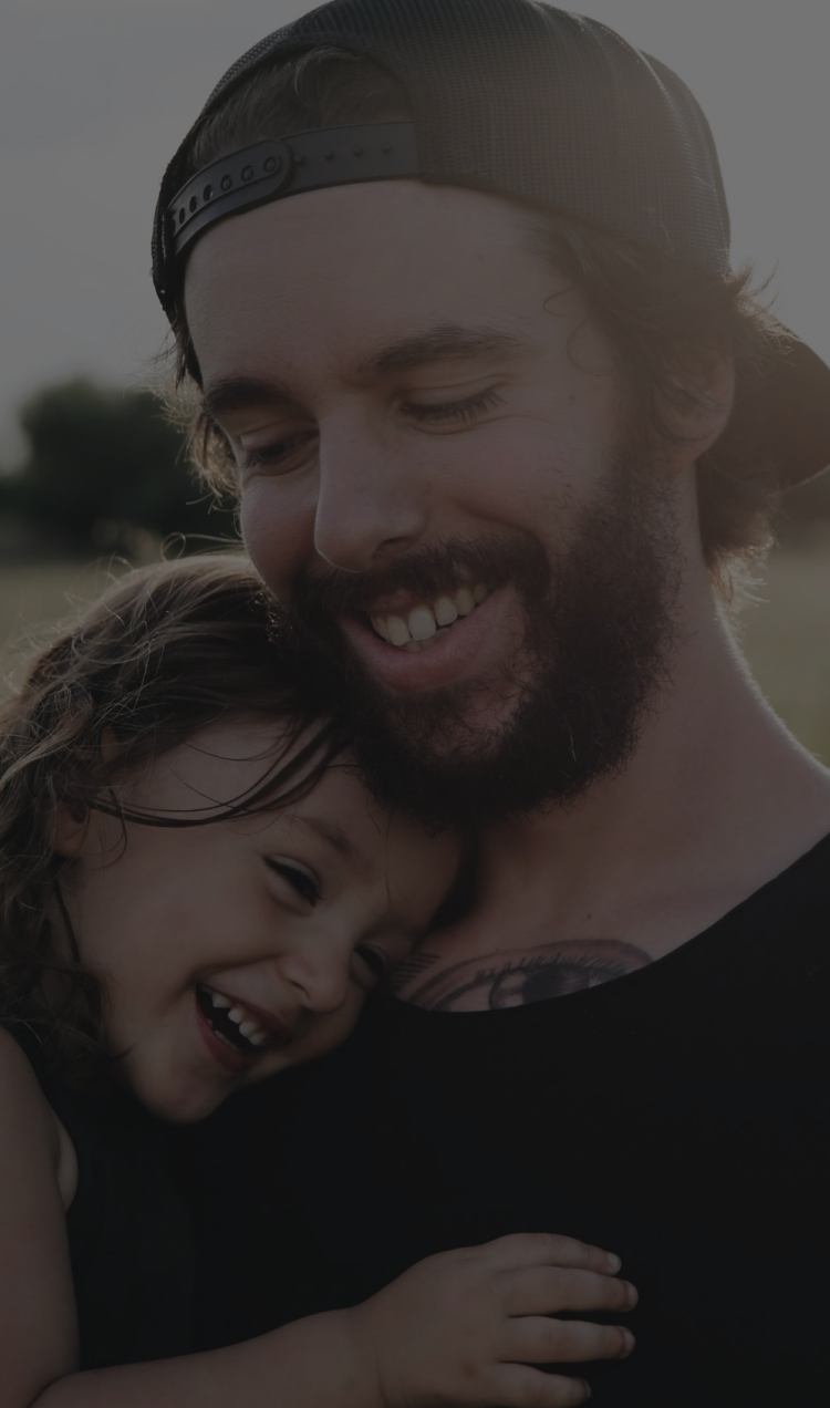 A father holds his young daughter as they both smile.