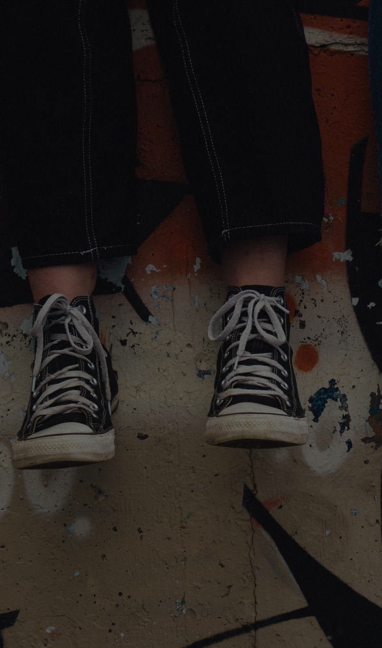 Two young people sitting on a graffiti concrete wall with their legs dangling down.