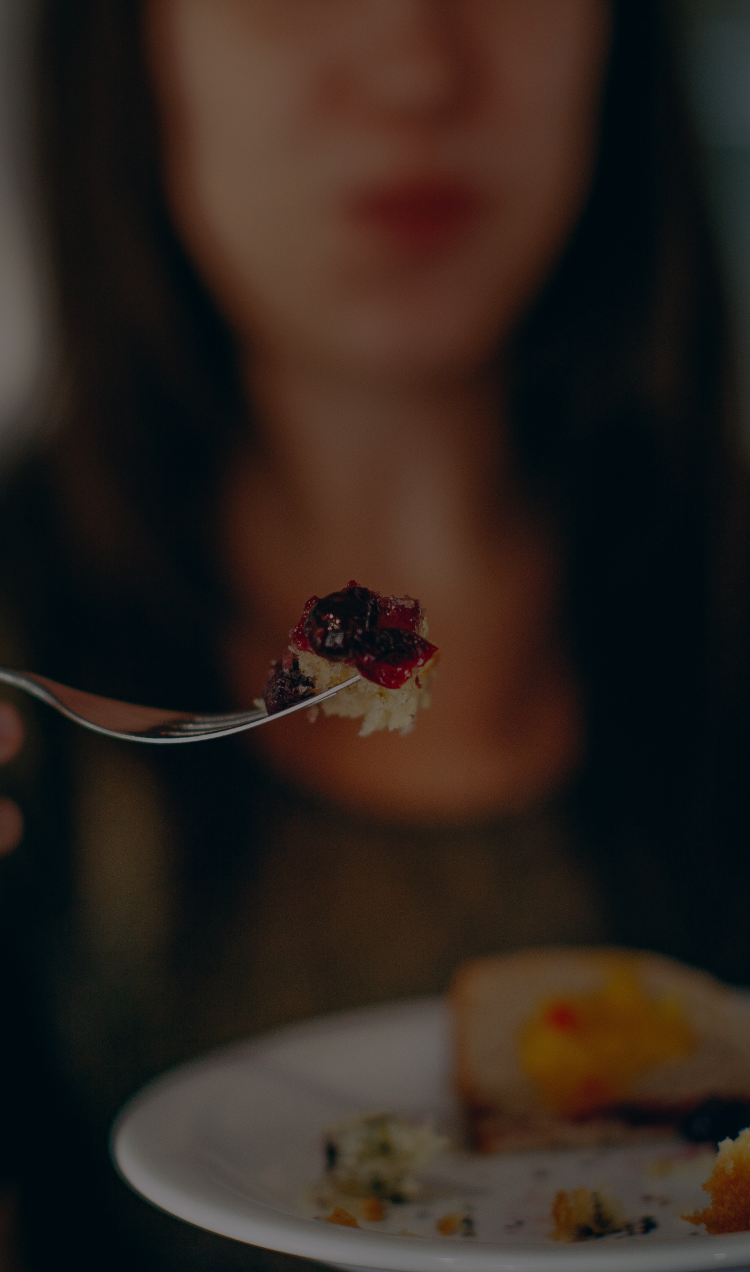 An out of focus woman holds a plate and a fork with food.