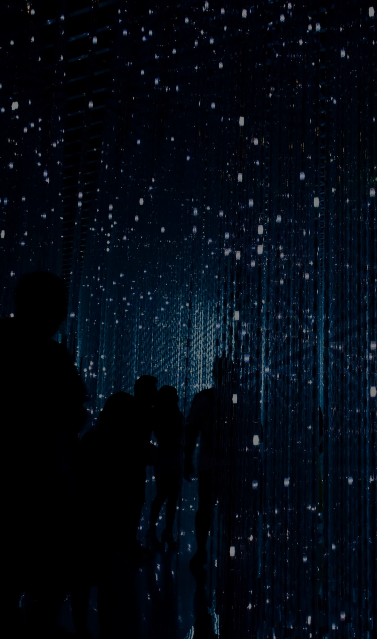 People standing in a dark blue room with mirrored walls as lights refract around them.