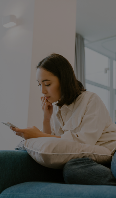 A woman scrolls on her phone from the couch.