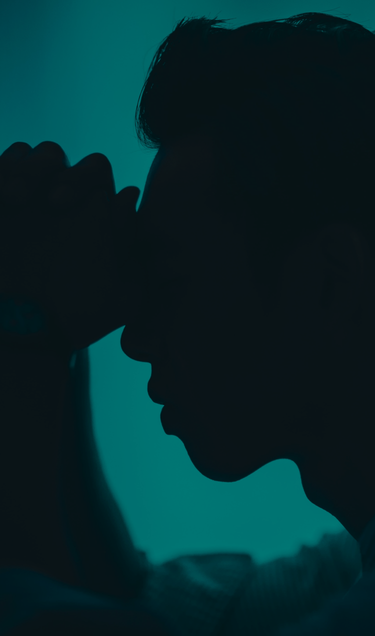 Silhouette of a man resting his hands to his forehead against a wall.