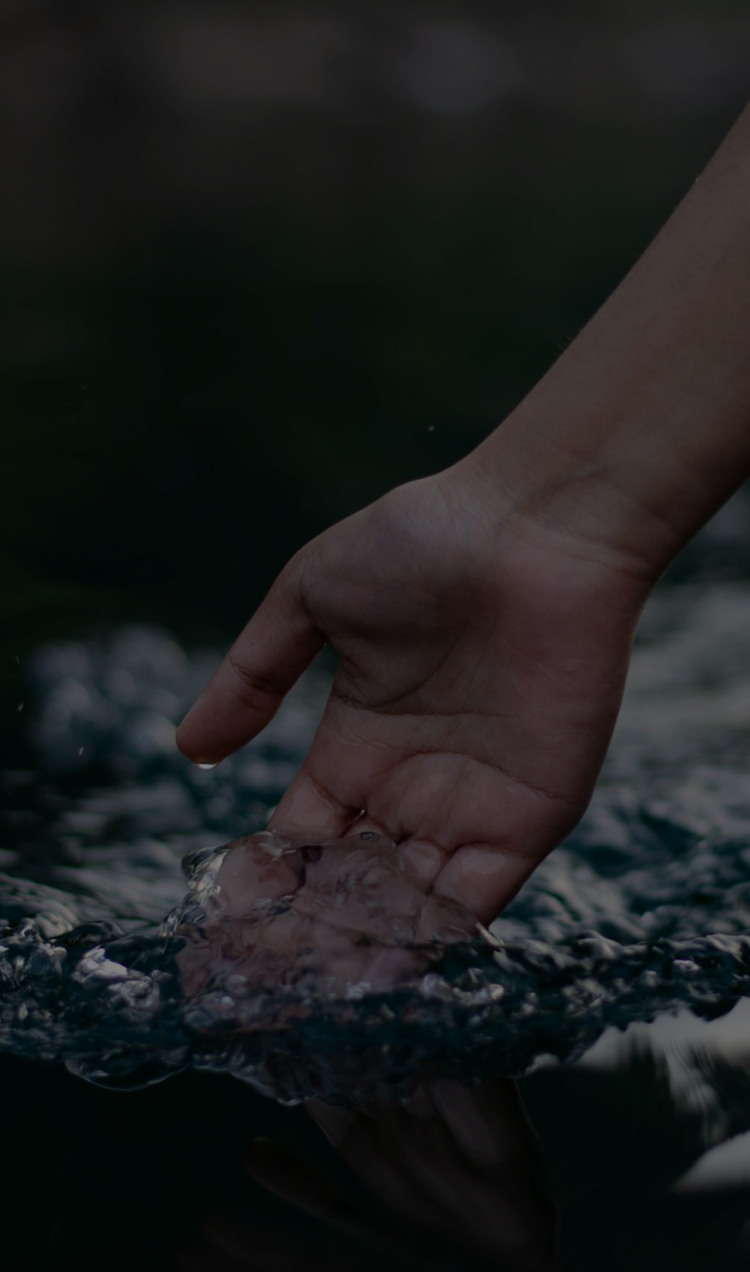 A hand dips into the water as a boat glides over a river.